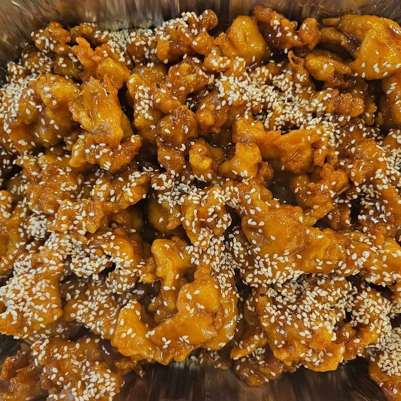 Close-up of Ho Mei Express Chinese Kitchen's sesame chicken, glistening with sauce and sprinkled with sesame seeds.