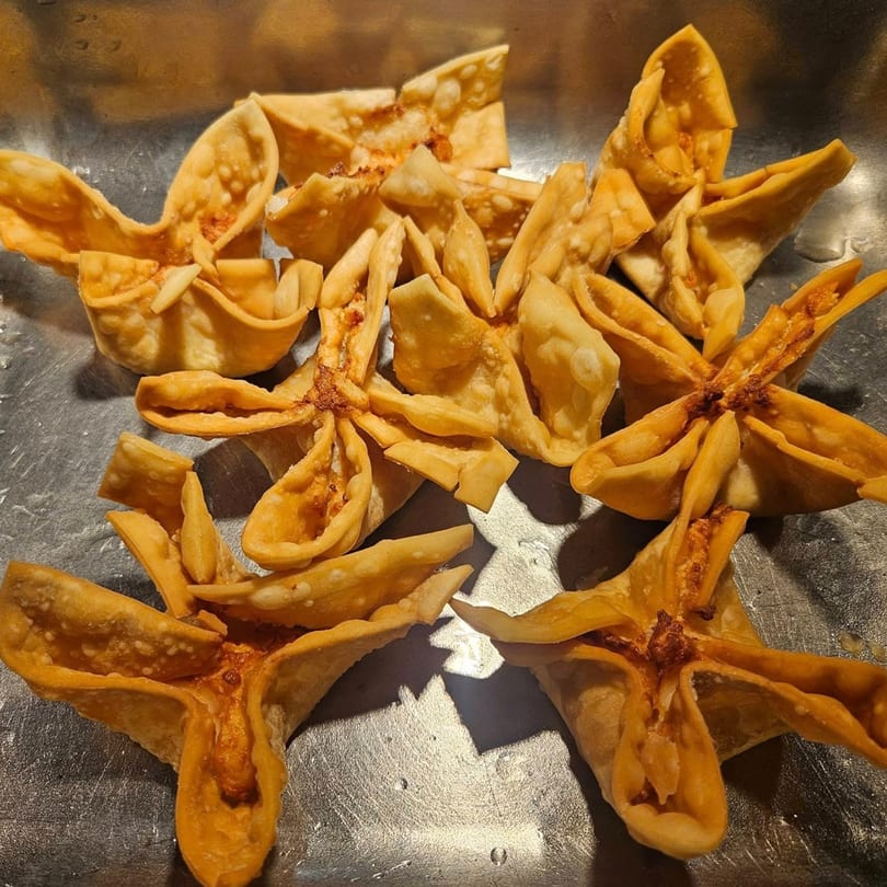 Crispy, golden-brown crab rangoon appetizers from Ho Mei Express Chinese Kitchen on a metal tray.